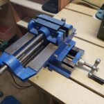 A blue and black cross-slide vise on a gunsmithing work bench.